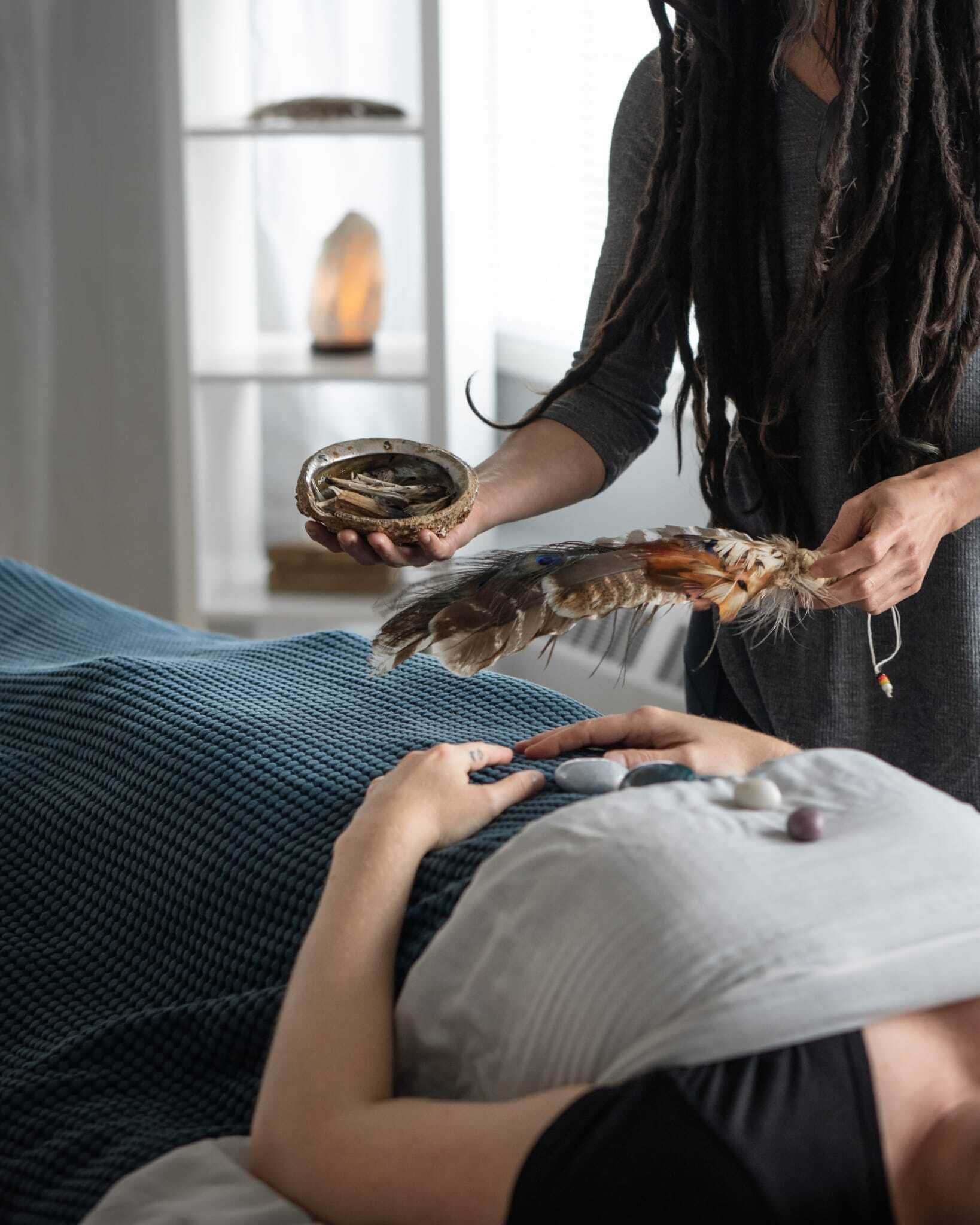 A person holding a bird of prey and a small bowl, in a room with a bed and a shelf with a candle.