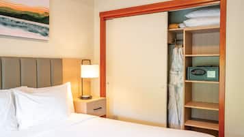 Habitación de hotel con cama, mesita de noche con lámpara, armario de madera y un cuadro en la pared.