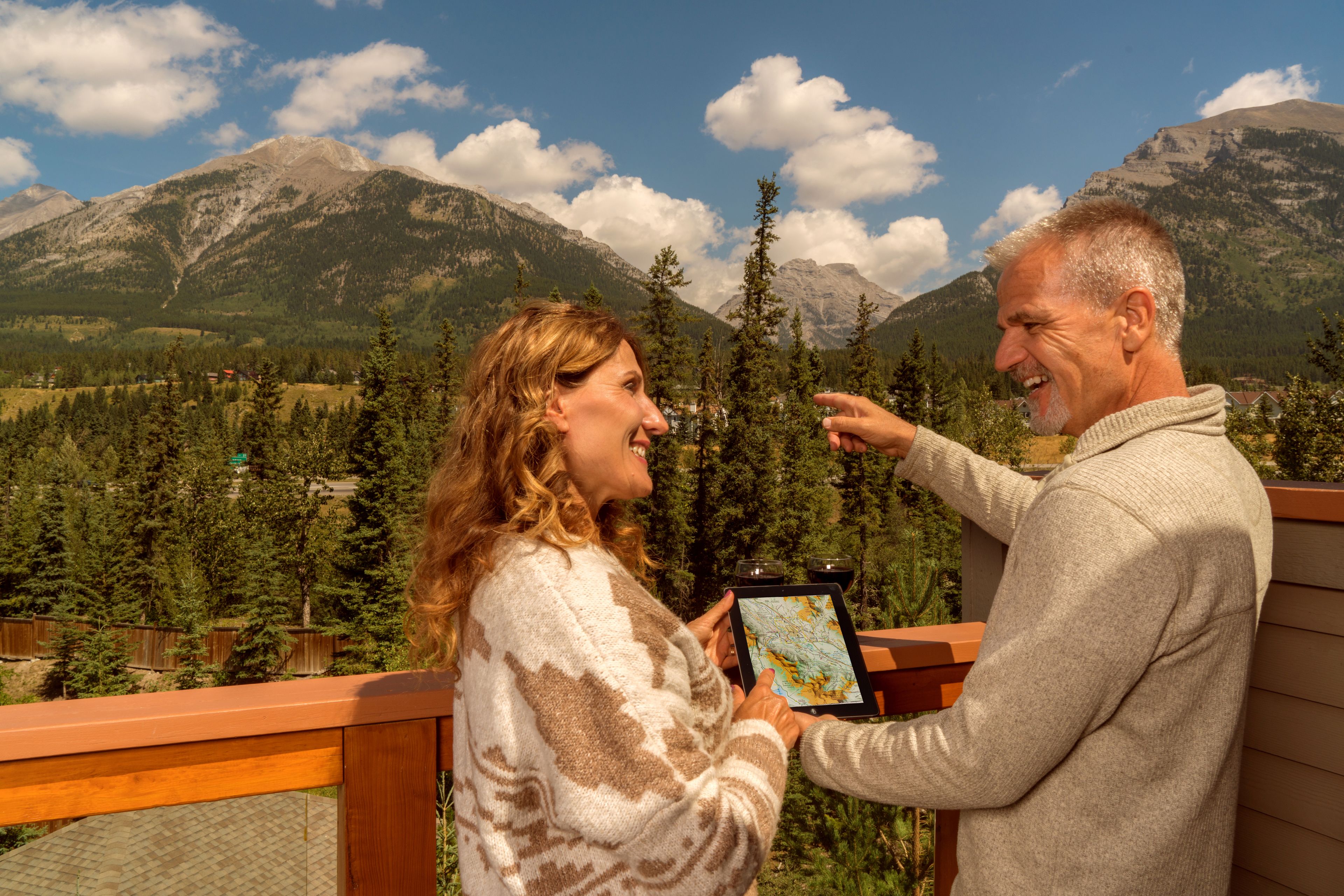 Un couple sur un balcon, tenant une tablette qui affiche une carte et surplombant un paysage montagneux.