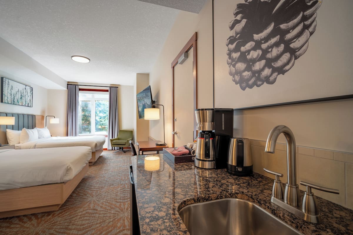 A hotel room with two beds, a kitchenette with a coffee maker, a sink, and a large pinecone artwork on the wall.