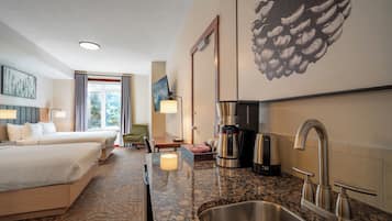 Een hotelkamer met twee bedden, een kitchenette met koffiezetapparaat, een spoelbak en een groot kunstwerk van een dennenappel aan de muur.