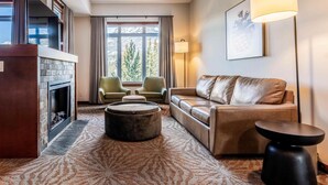 A living room with a fireplace, leather sofa, two armchairs, a round ottoman, and a floor lamp.