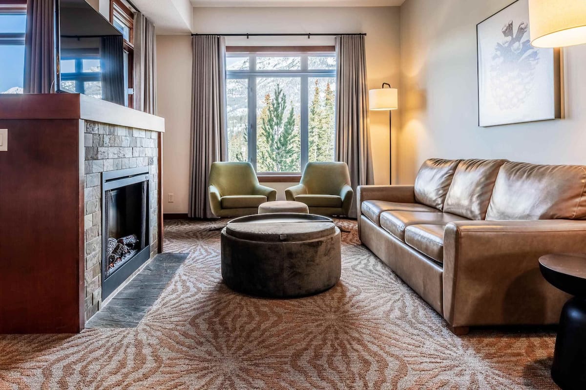 A living room with a fireplace, leather sofa, two armchairs, a round ottoman, and a floor lamp.