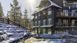 A multi-story building with a ski lift, a pool area with hot tubs, and snow-covered surroundings.