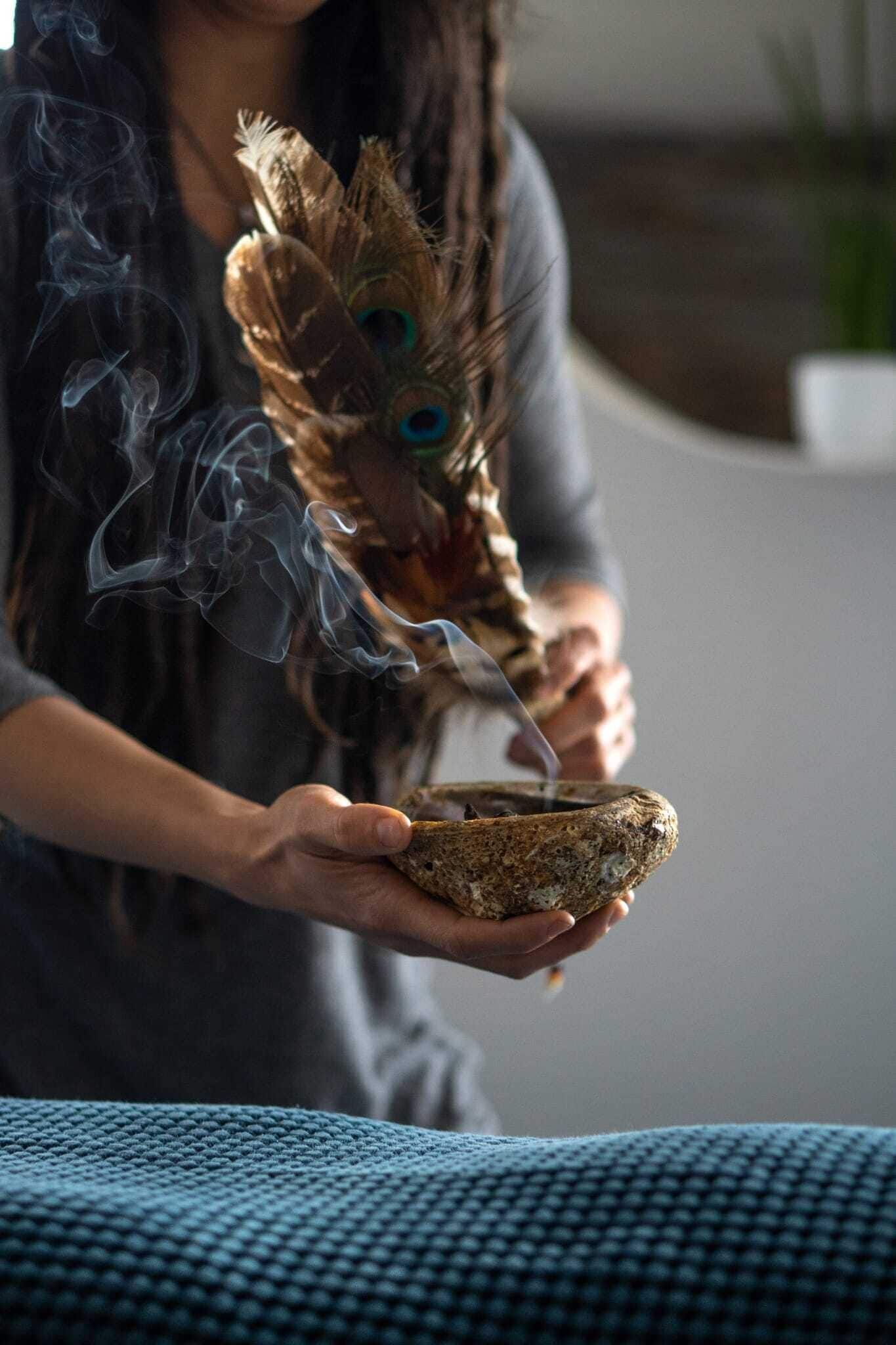 Una persona sosteniendo un tazón con humo y una pluma de pavo real.