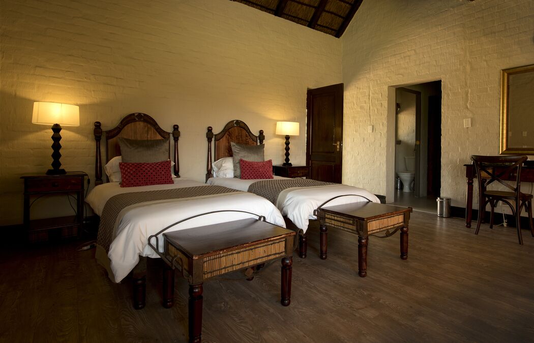 A double room with two beds, wooden headboards, and bedside tables with lamps.