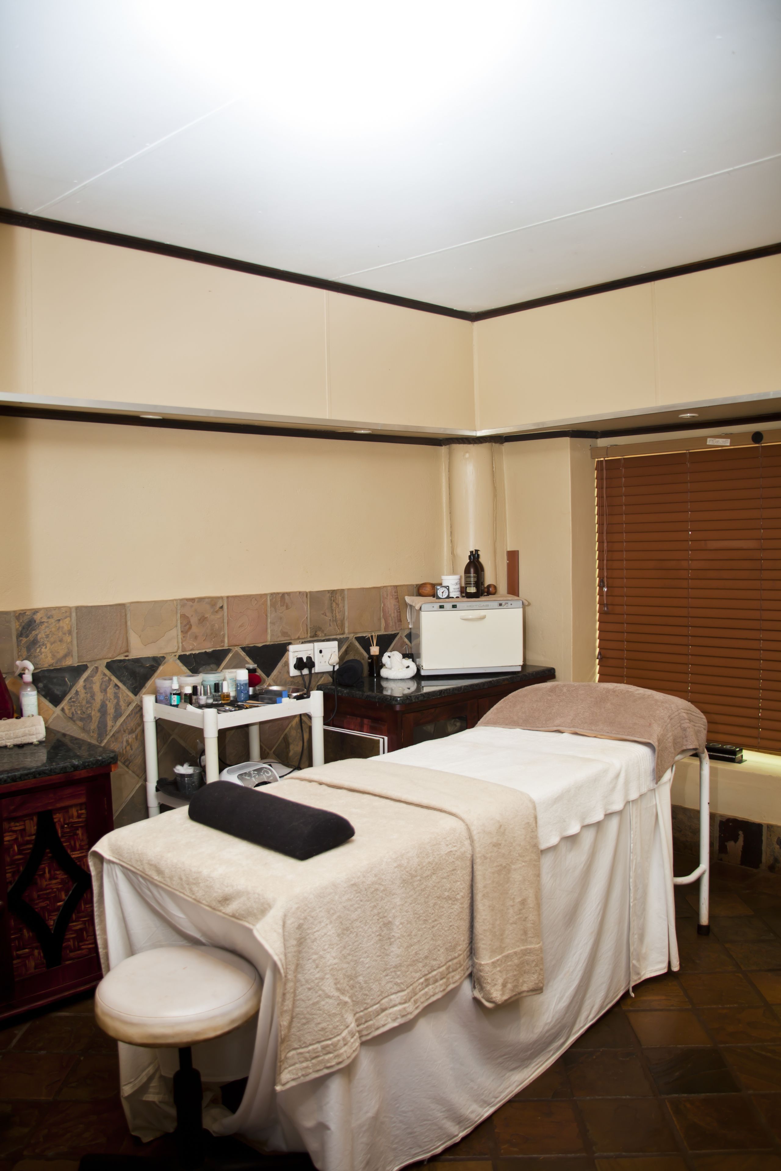 A room with a bed, a small table with toiletries, a chair, and a window with blinds.