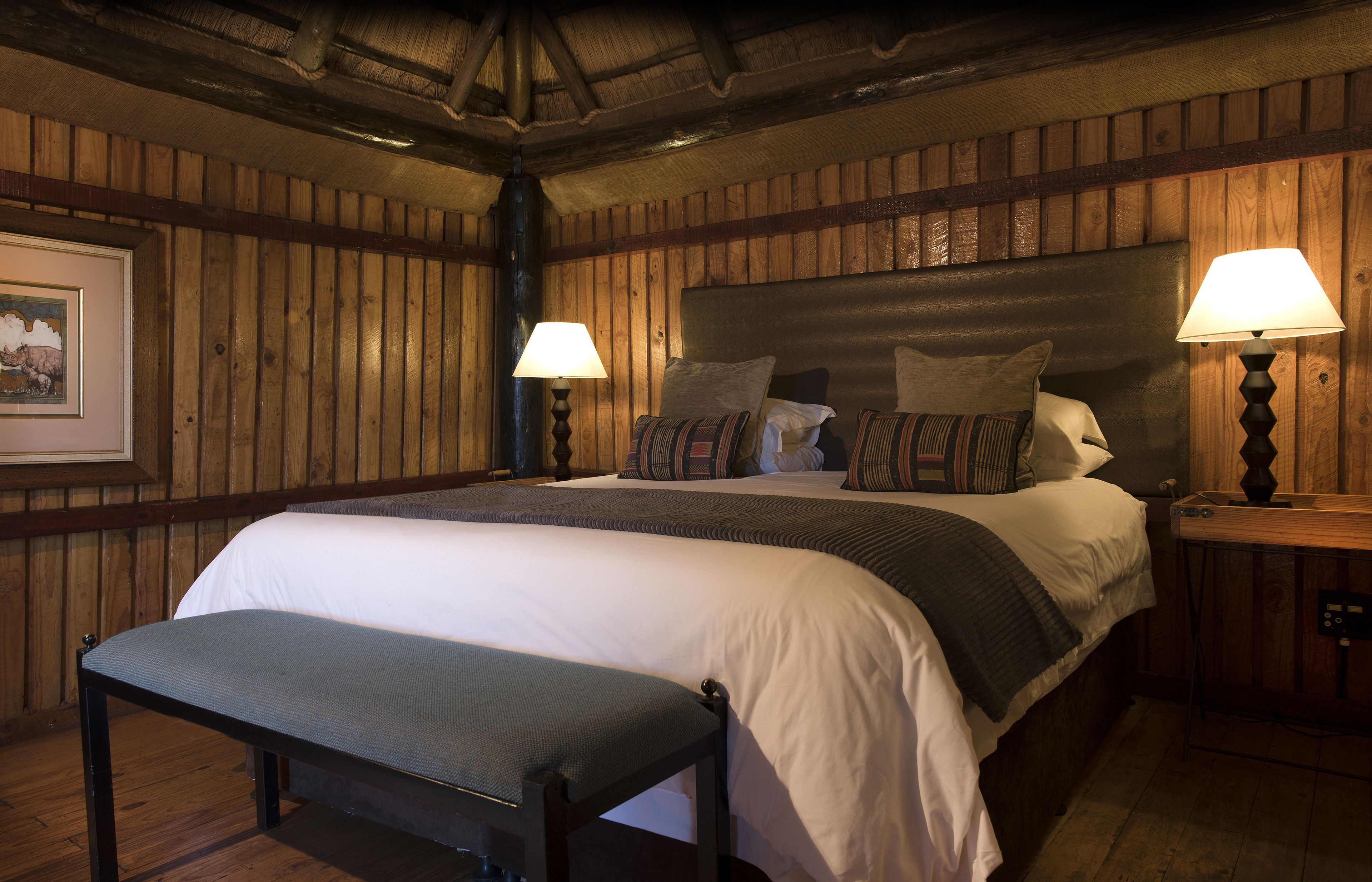 A wooden-paneled bedroom with a large bed, two bedside lamps, and a bench.