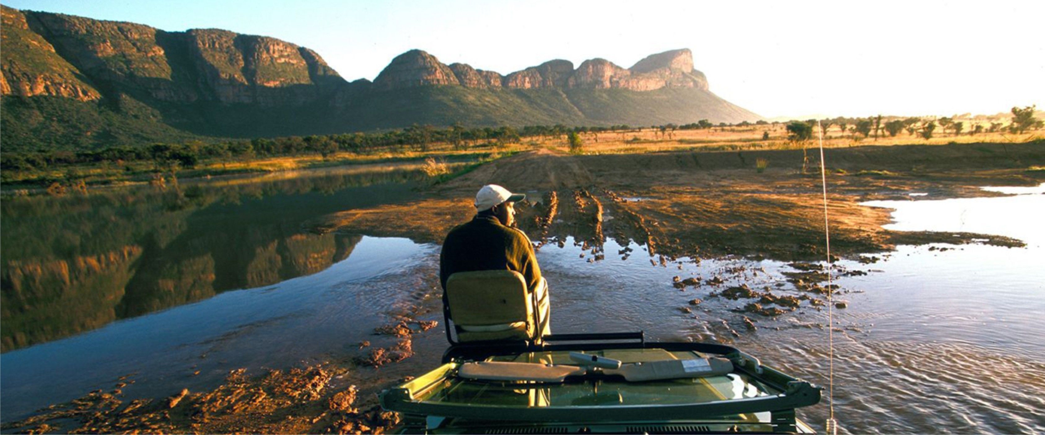 A person in a boat on a calm river with mountains in the background.