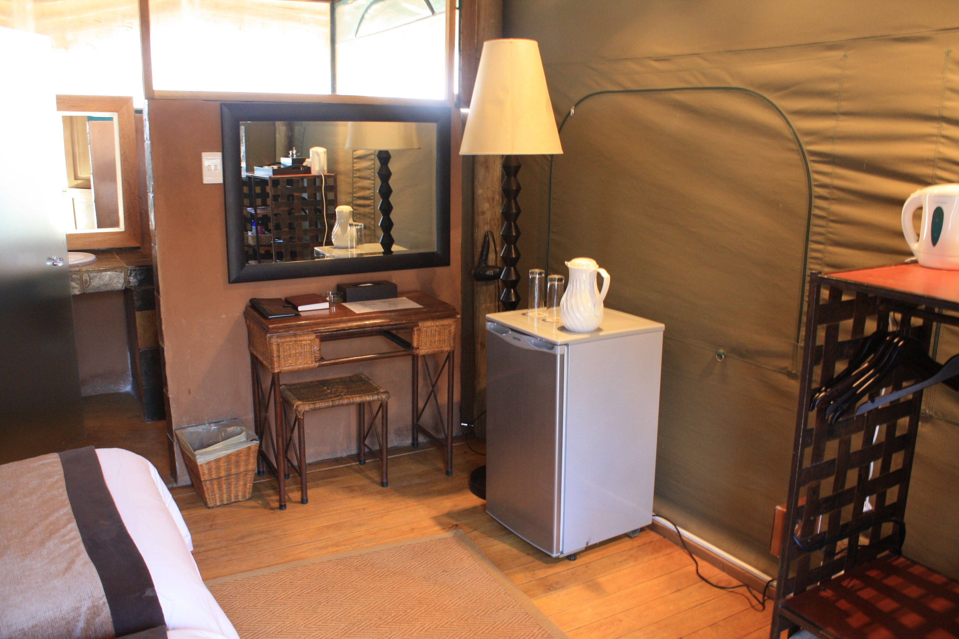 Une chambre d’hôtel de taille réduite, comprenant un lit, un petit bureau, un réfrigérateur, une lampe et une chaise.