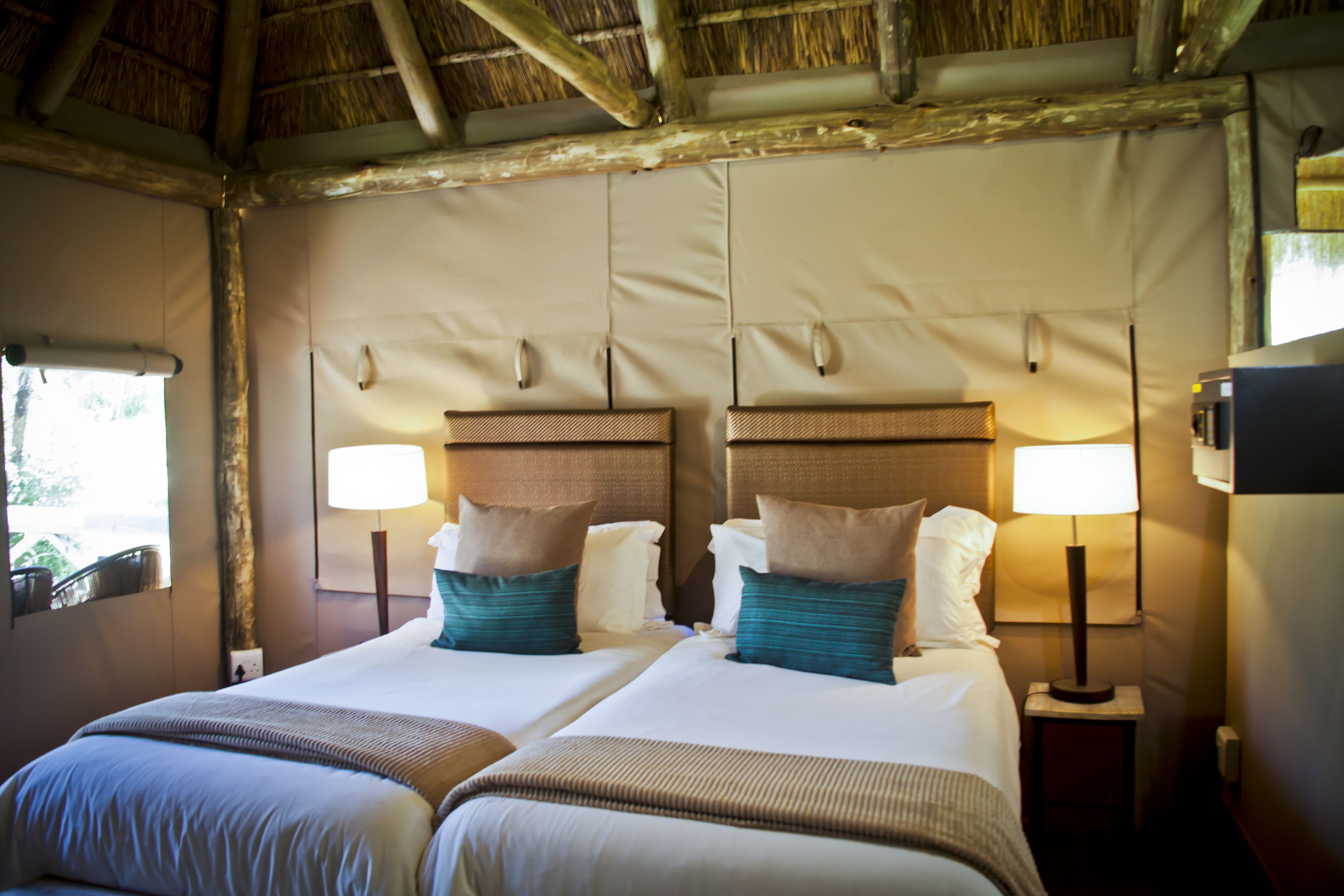 A hotel room with two beds, each with a headboard, bedside lamps, and pillows.