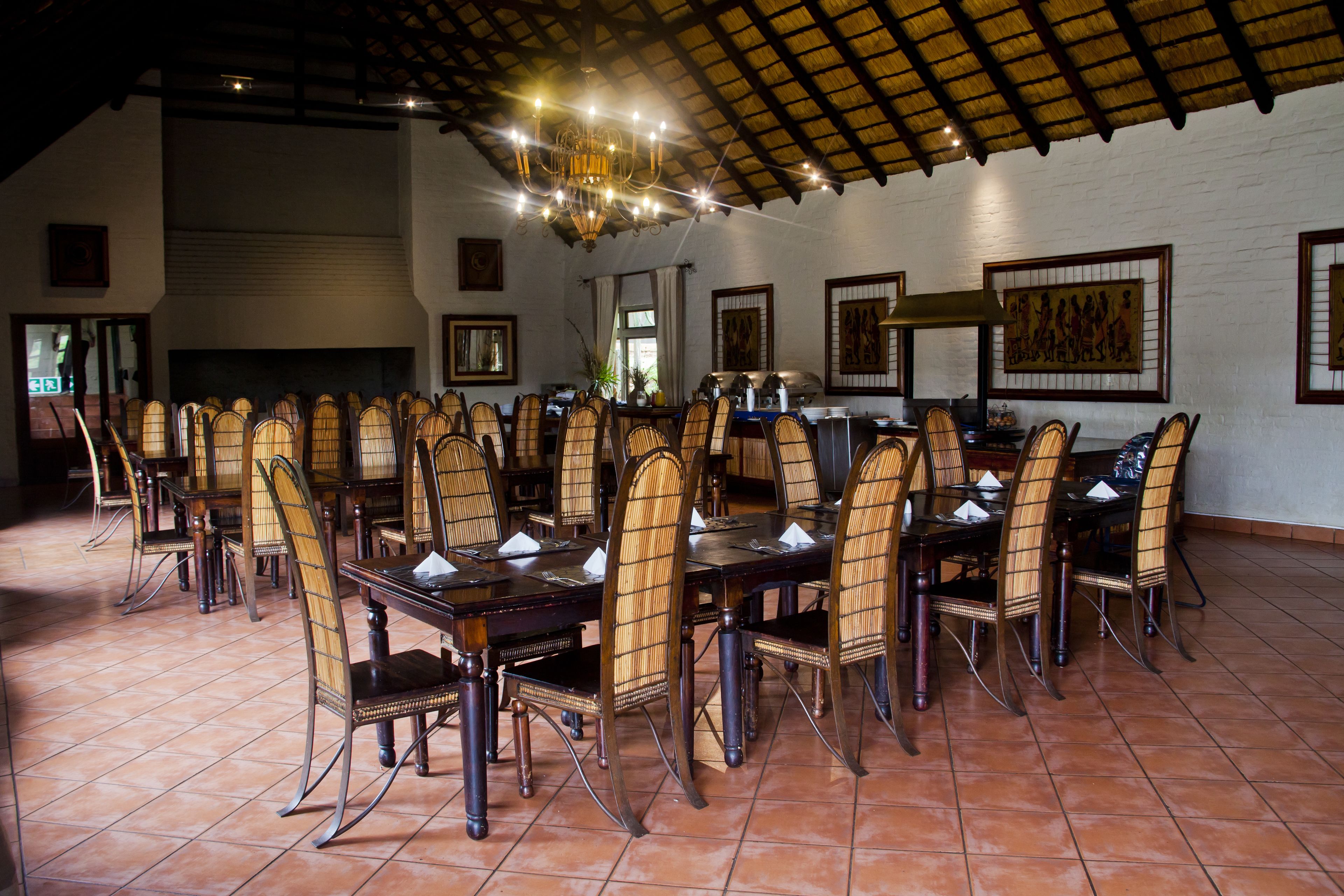 Un comedor amplio con mesas largas y sillas de mimbre, un techo alto con vigas a la vista y obras de arte enmarcadas en las paredes.