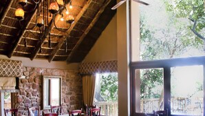 A cozy interior with a stone wall, wooden ceiling, and large windows. - Entabeni Mountain Lodges (Mookgopong)