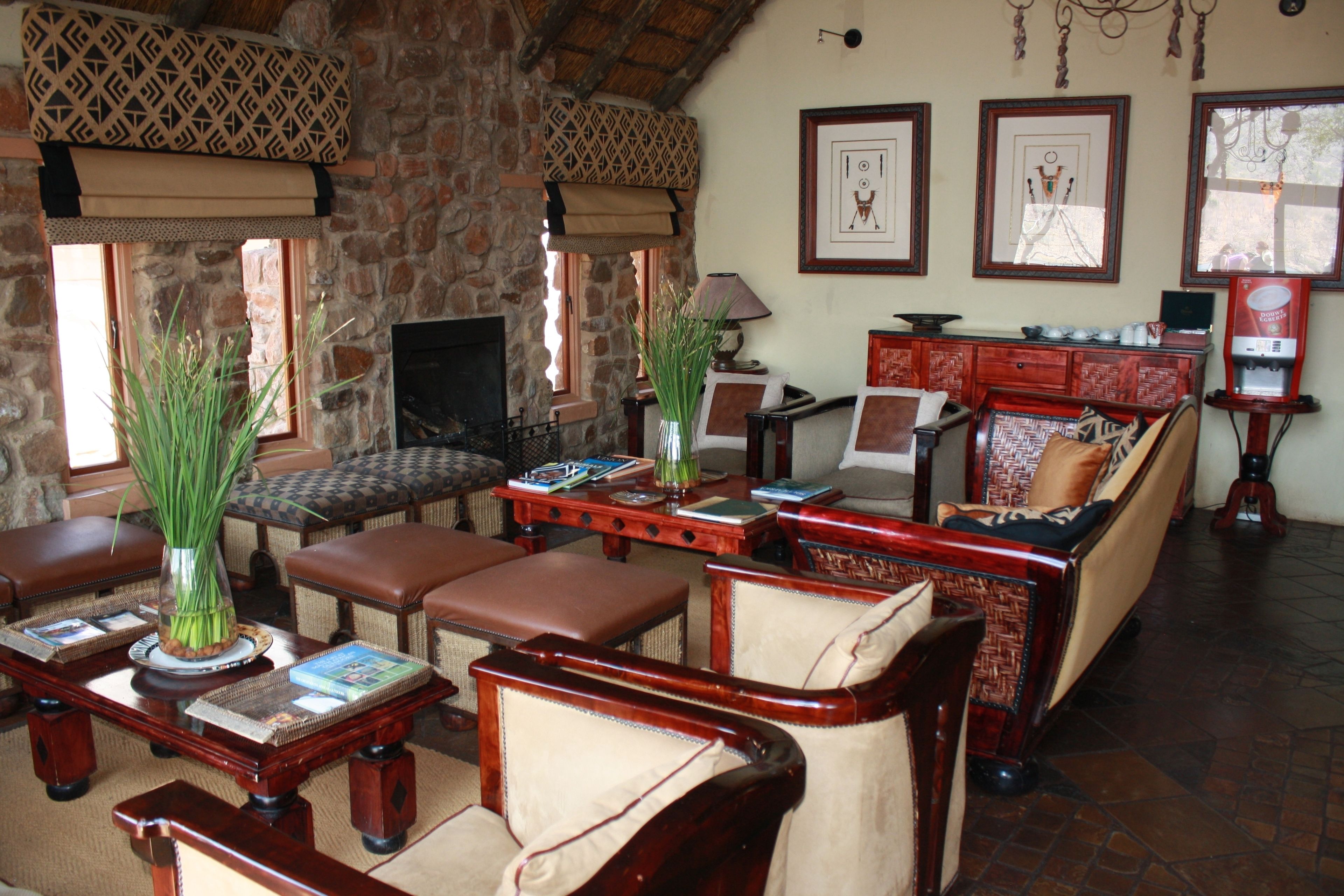 A cozy living room with stone walls, leather furniture, and a fireplace. There are framed pictures on the wall and a coffee machine.