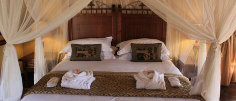 A double bed with a canopy, two pillows with decorative patterns, and two towels folded on the bed.