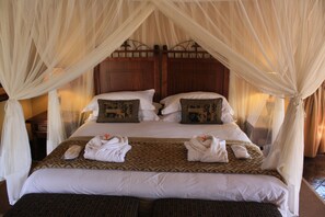 A double bed with a canopy, two pillows with decorative patterns, and two towels folded on the bed.