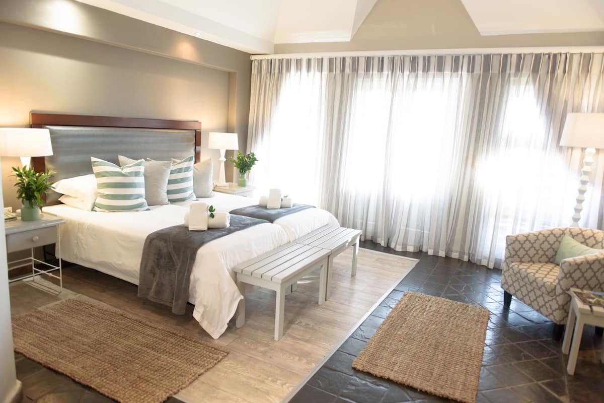 A bedroom with a bed, bedside tables, a bench, a chair, and a large window with curtains.