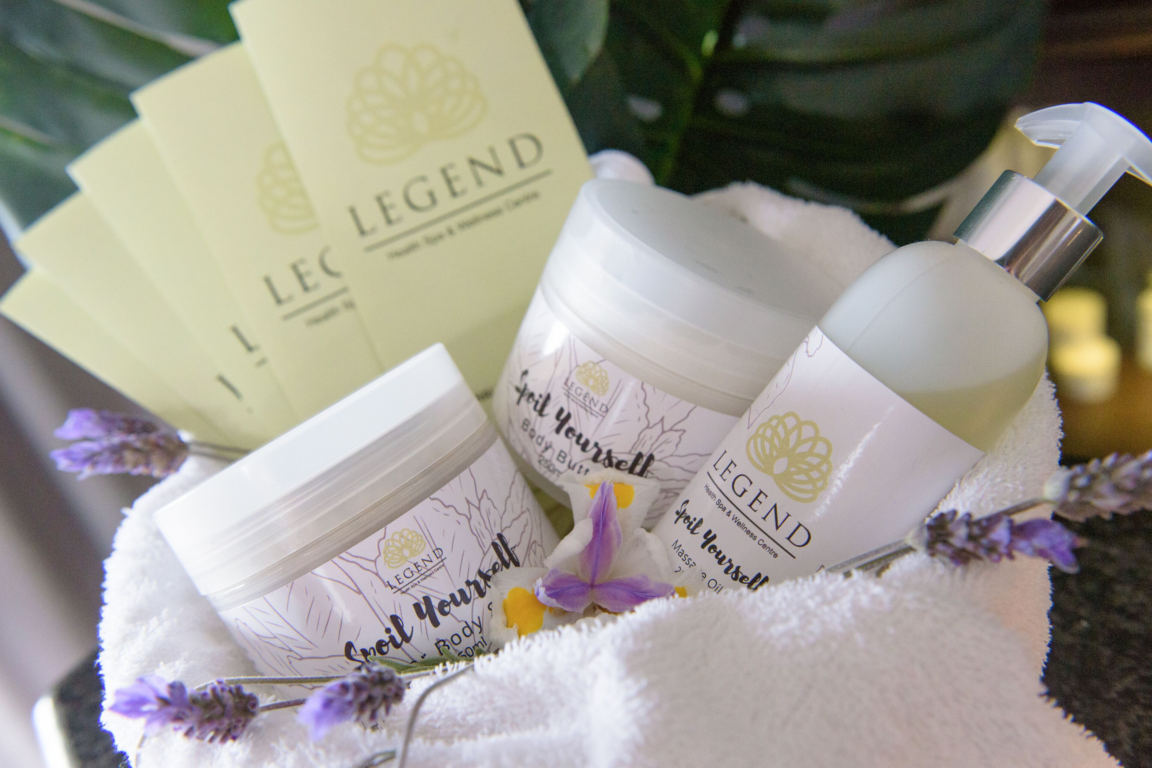 Un conjunto de productos para el cuidado de la piel etiquetados como 'Legend' en una cesta blanca, mullida y acolchada con flores de lavanda.