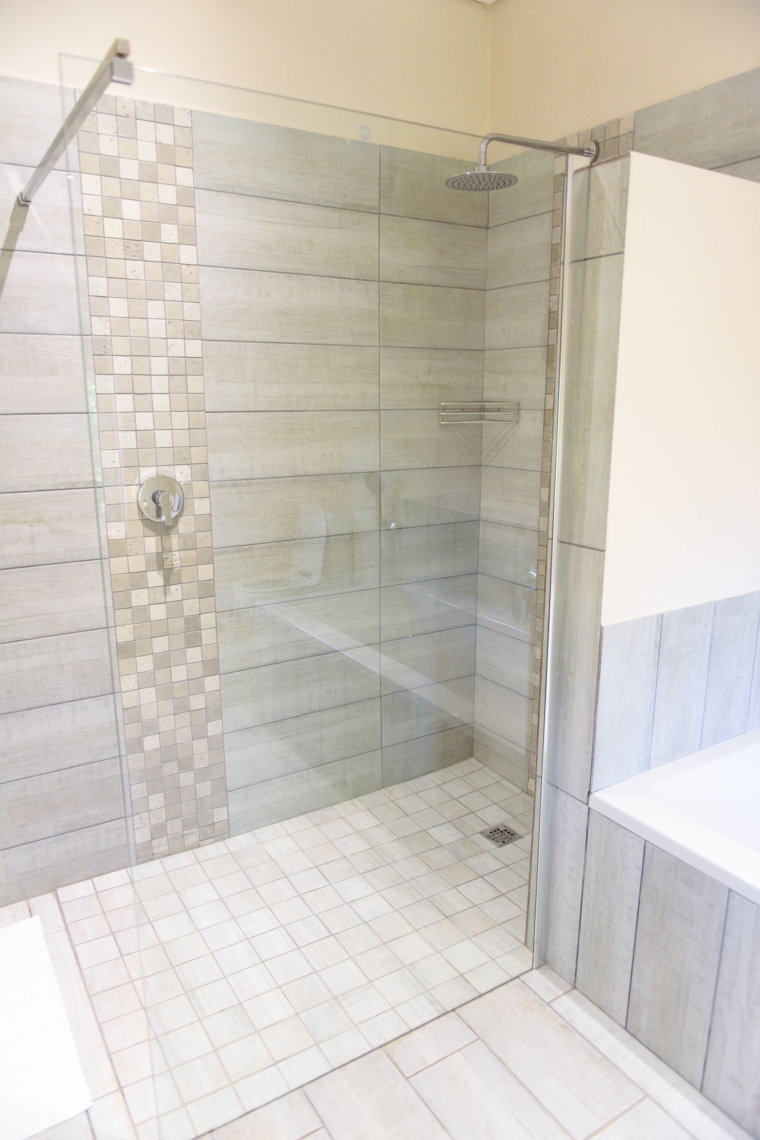 A modern bathroom with a glass shower enclosure, tiled walls, and a white sink area.