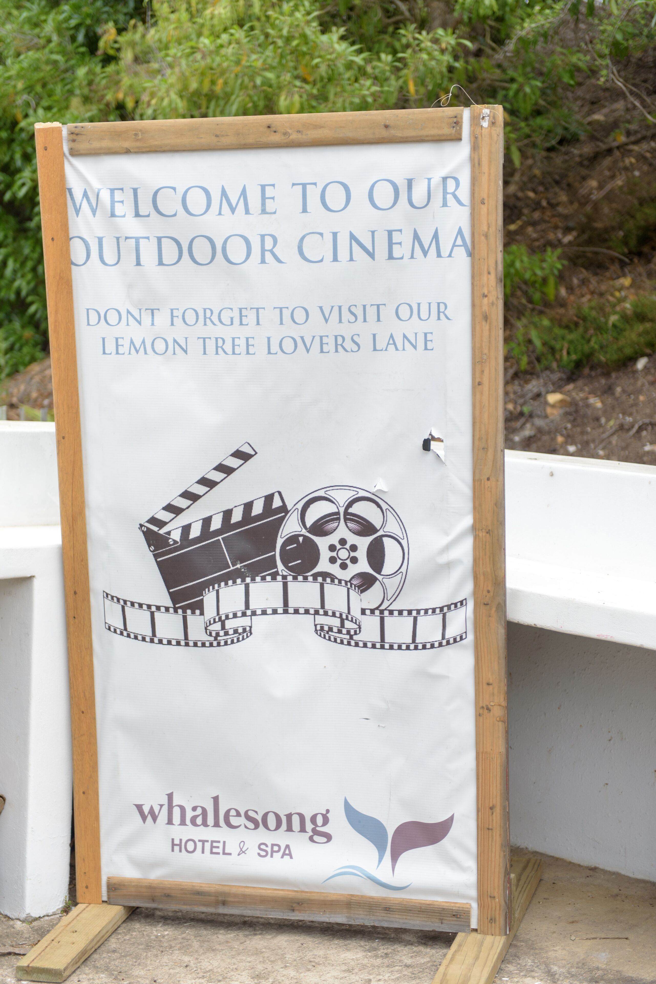 Une enseigne indiquant l’emplacement d’un cinéma en plein air à l’hôtel et au spa Whalesong, avec une illustration représentant une claquette de cinéma et un bobine de film.