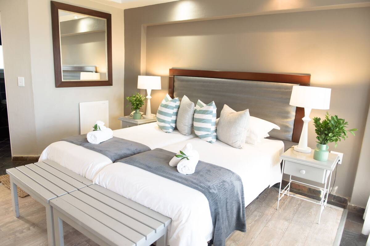 A neatly arranged hotel room with a large bed, two bedside tables, a bench, a mirror, and a potted plant.