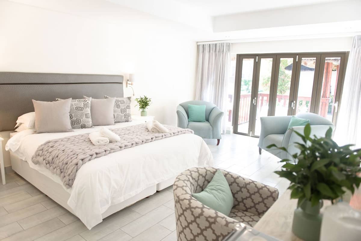 A hotel room with a bed, two armchairs, a sofa, a small table, and a potted plant.