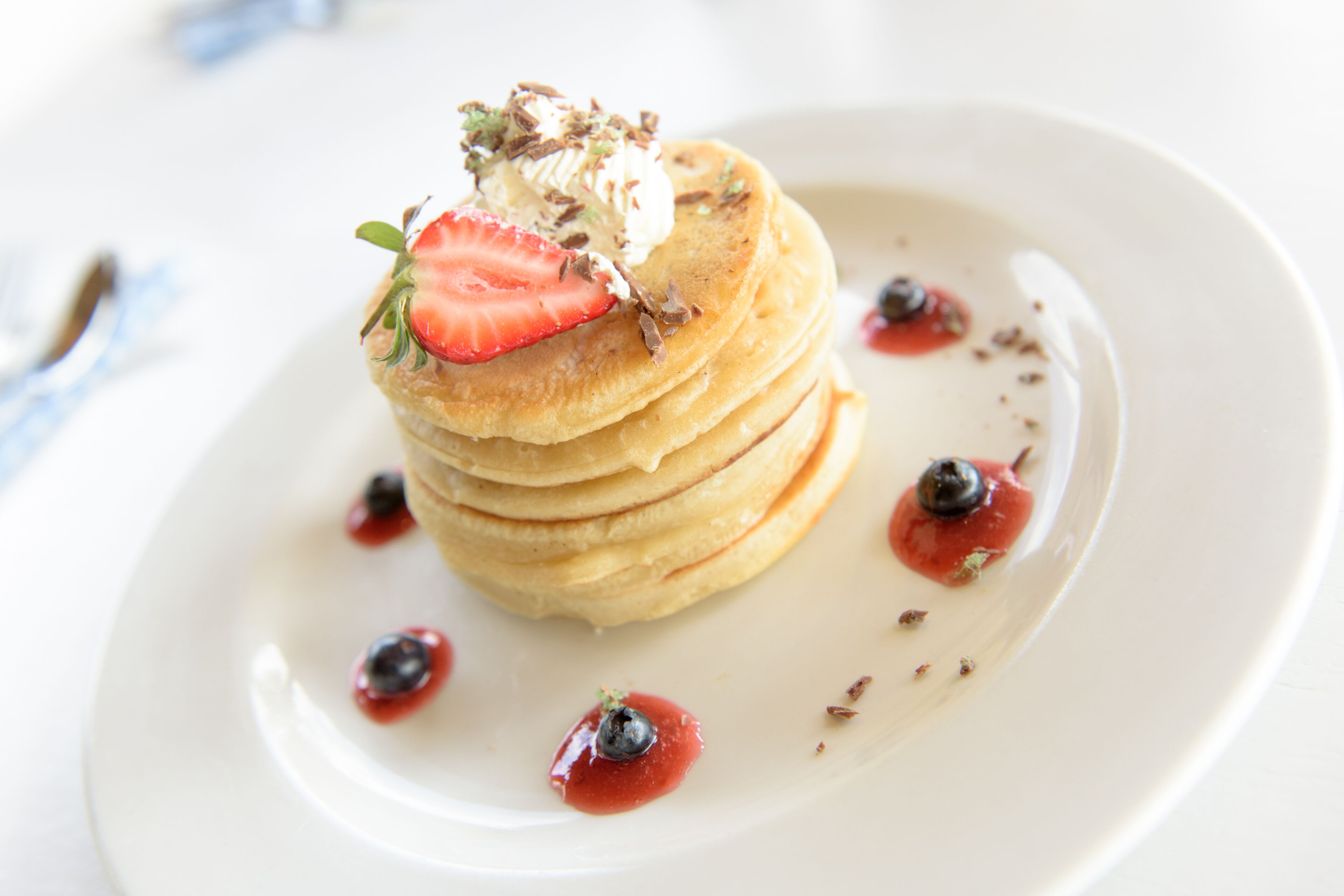 A stack of pancakes with strawberries and blueberries on a white plate.