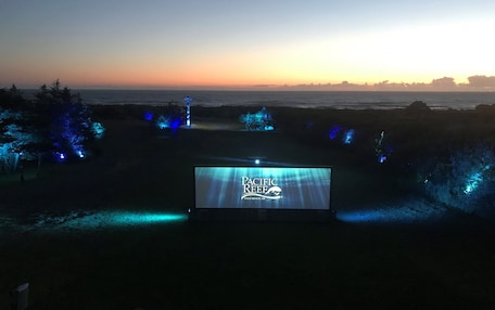 A large outdoor screen displaying "Pacific Reef" with a view of the ocean and trees illuminated by blue lights.