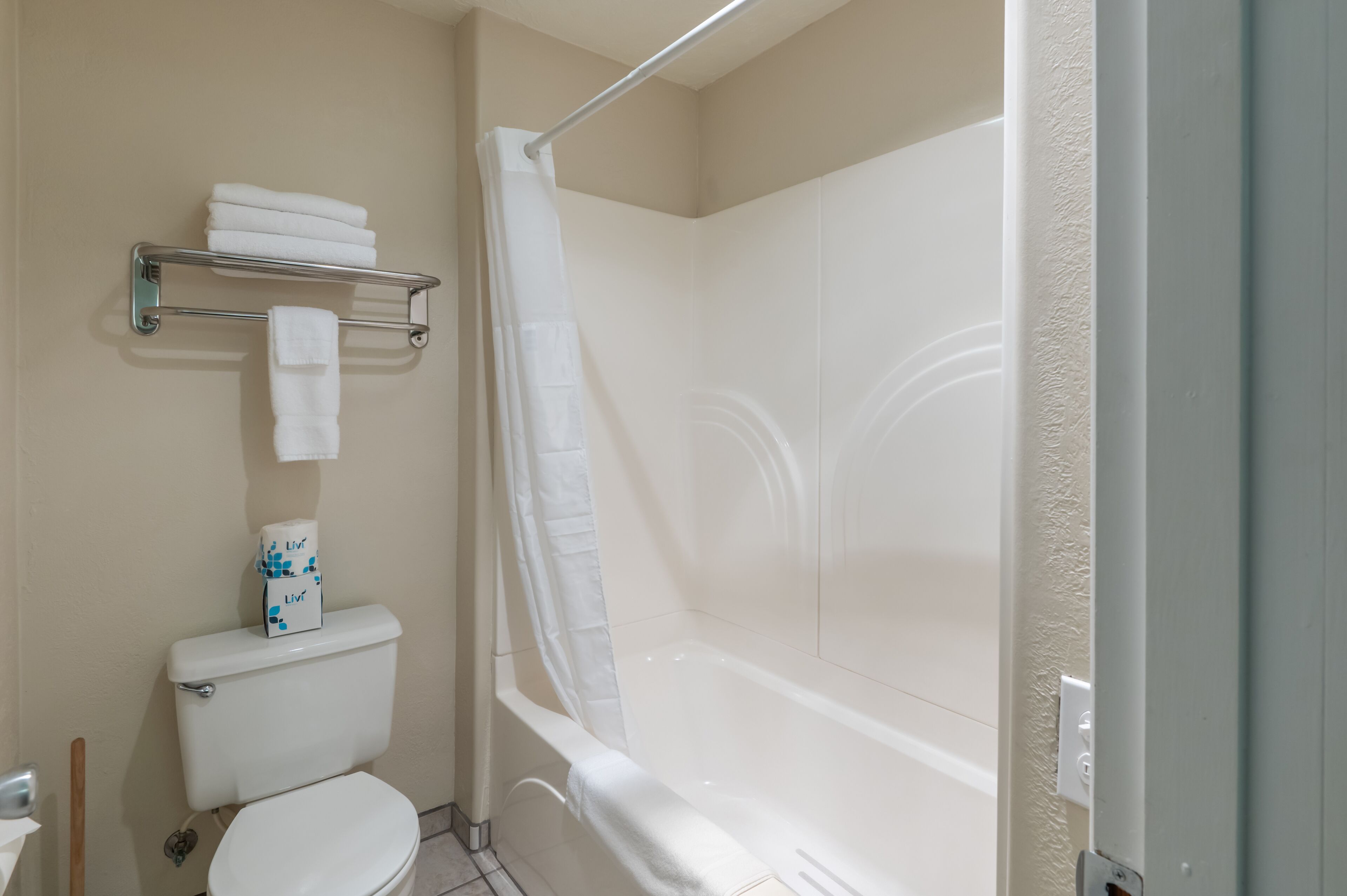 A bathroom with a toilet, a shower with a curtain, and a shelf with towels.