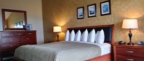 Una habitación de hotel con una cama grande, cabecera de madera, dos mesitas de noche con lámparas, un aparador y tres cuadros enmarcados en la pared.