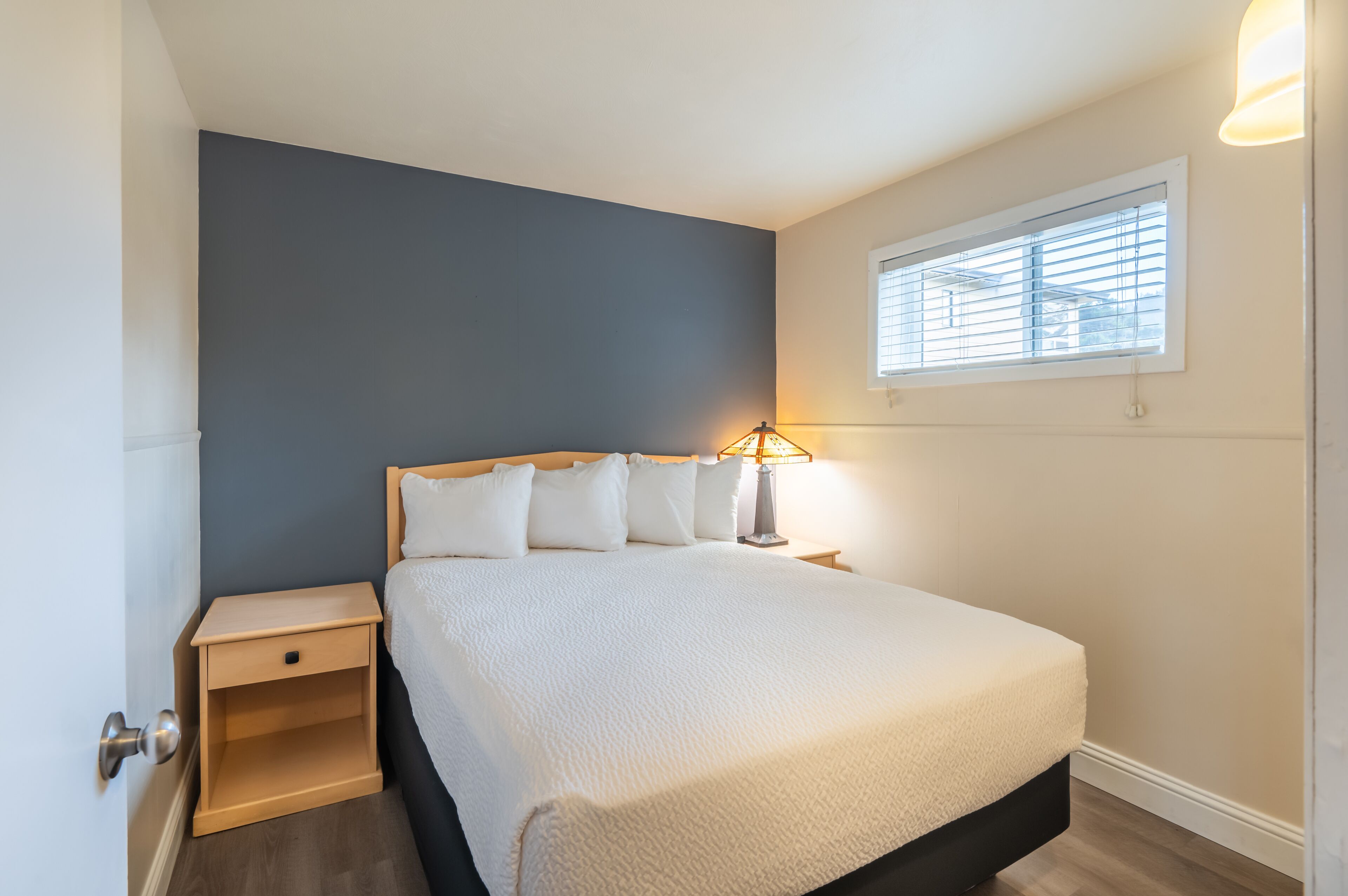 Un dormitorio con cama, mesitas de noche, una ventana con persianas y una lámpara.