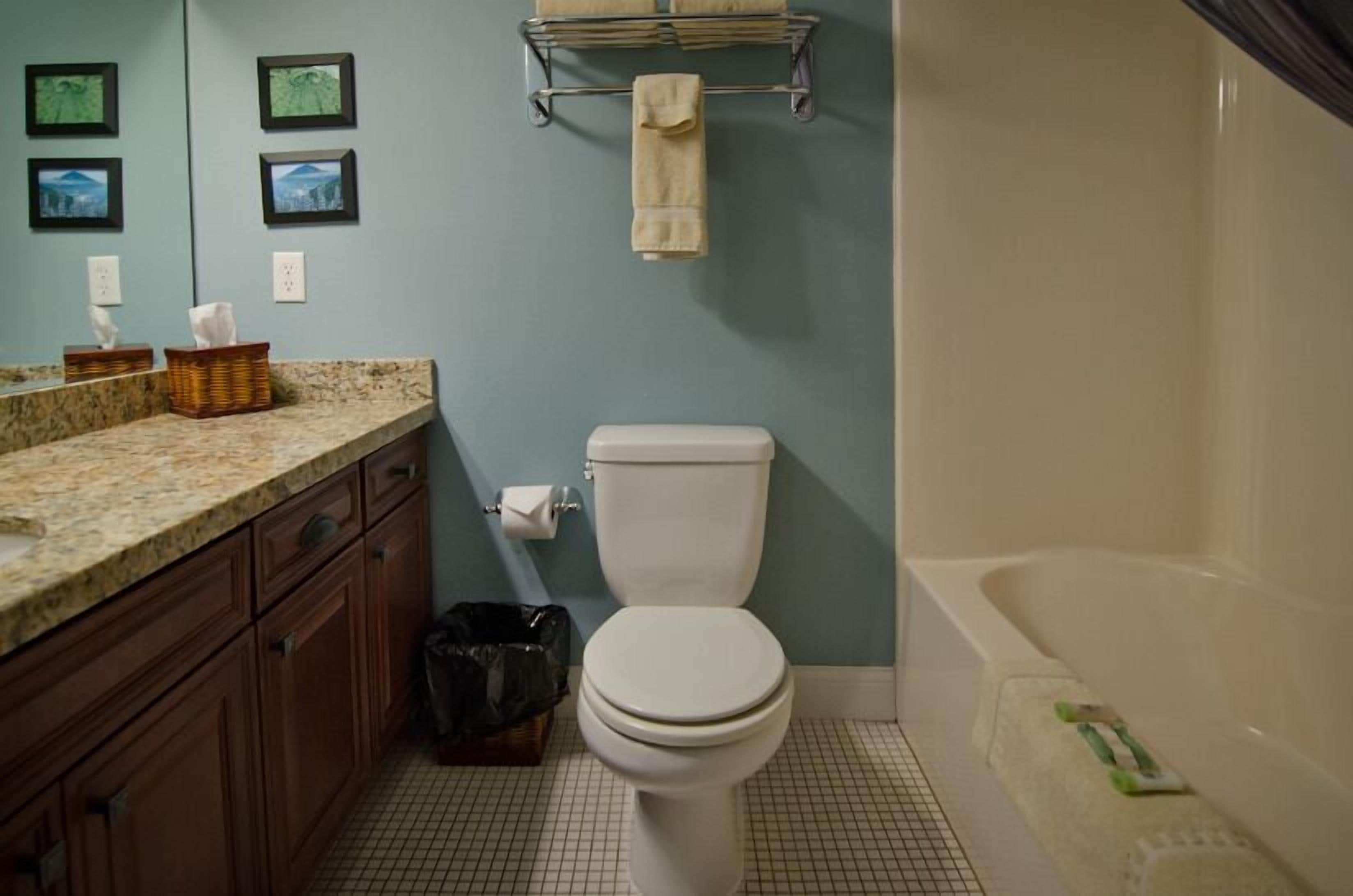 A bathroom with a toilet, sink, and bathtub. There are towels hanging on a rack, a trash bin, and a basket on the counter.