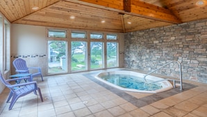 A spa area with a stone wall, a hot tub, and two Adirondack chairs. - Pacific Reef Hotel & Light Show (Gold Beach)