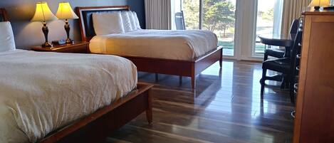 Ein Hotelzimmer mit zwei Betten, einem Schreibtisch, einem Stuhl und einem großen Fenster mit Vorhängen.