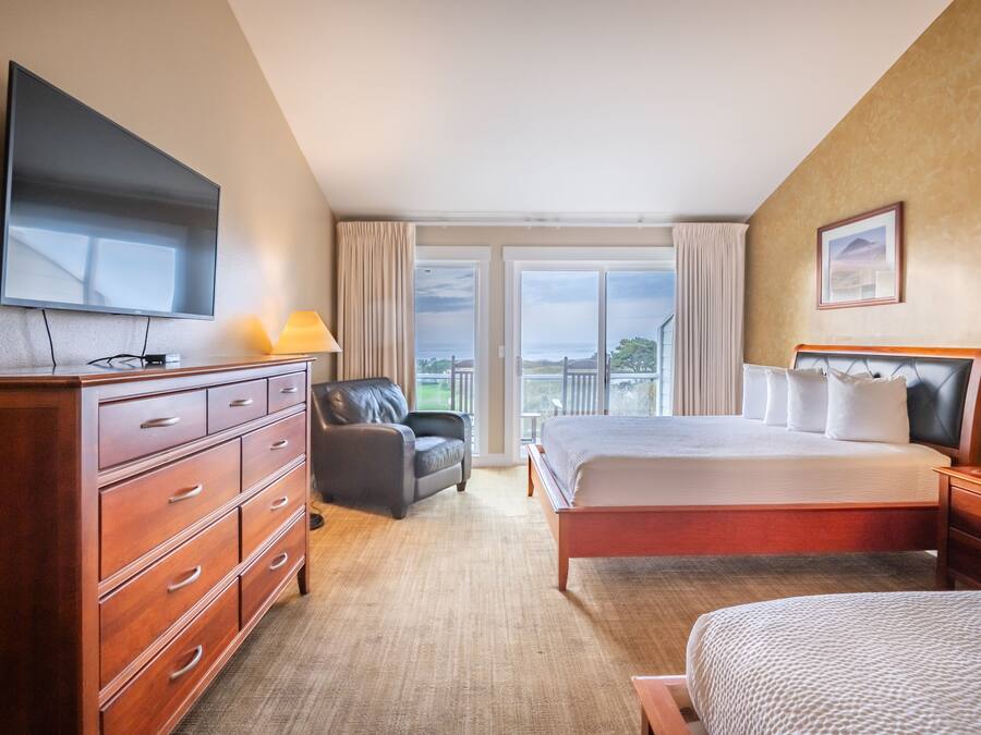 A hotel room with a large bed, a TV, a desk, a chair, and a view of the outdoors.