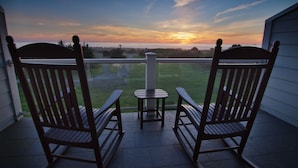 Two rocking chairs on a balcony with a view of a sunset over a body of water. - Pacific Reef Hotel & Light Show (Gold Beach)
