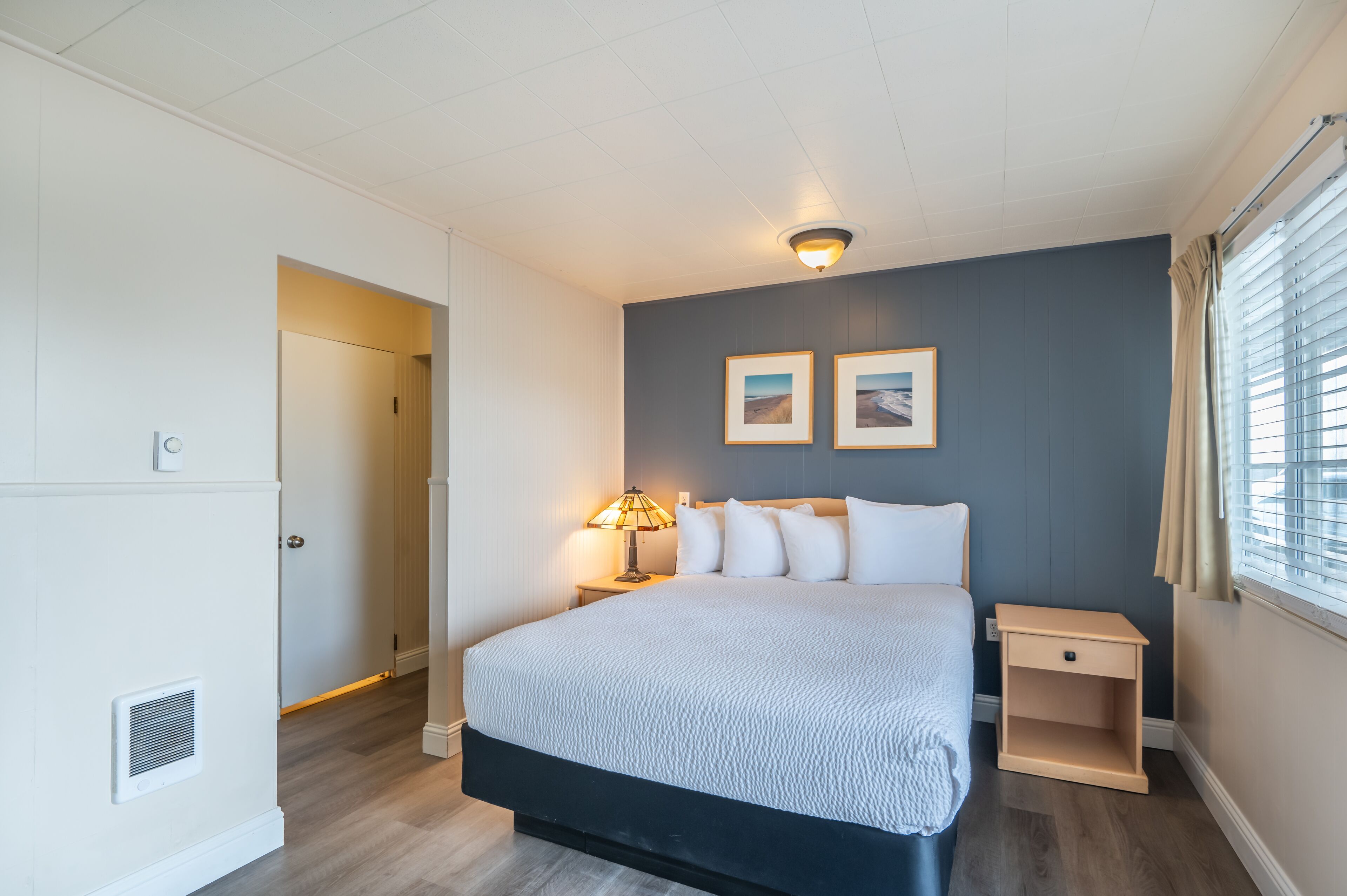 Un dormitorio con una cama grande, una mesita de noche, una lámpara y dos cuadros en la pared.
