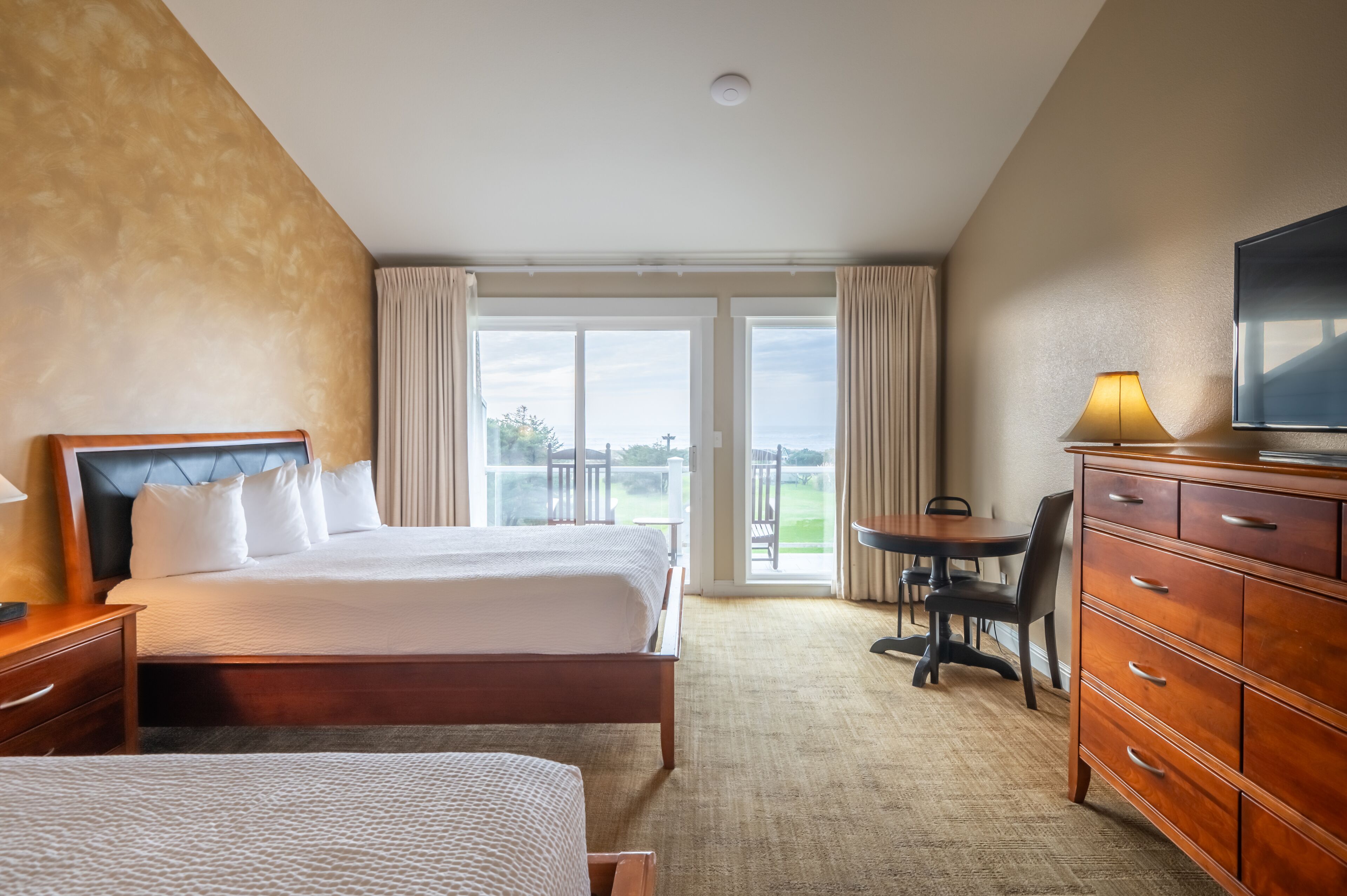 Quarto de hotel com uma cama grande, uma mesa com cadeira, televisão e vista para o exterior.