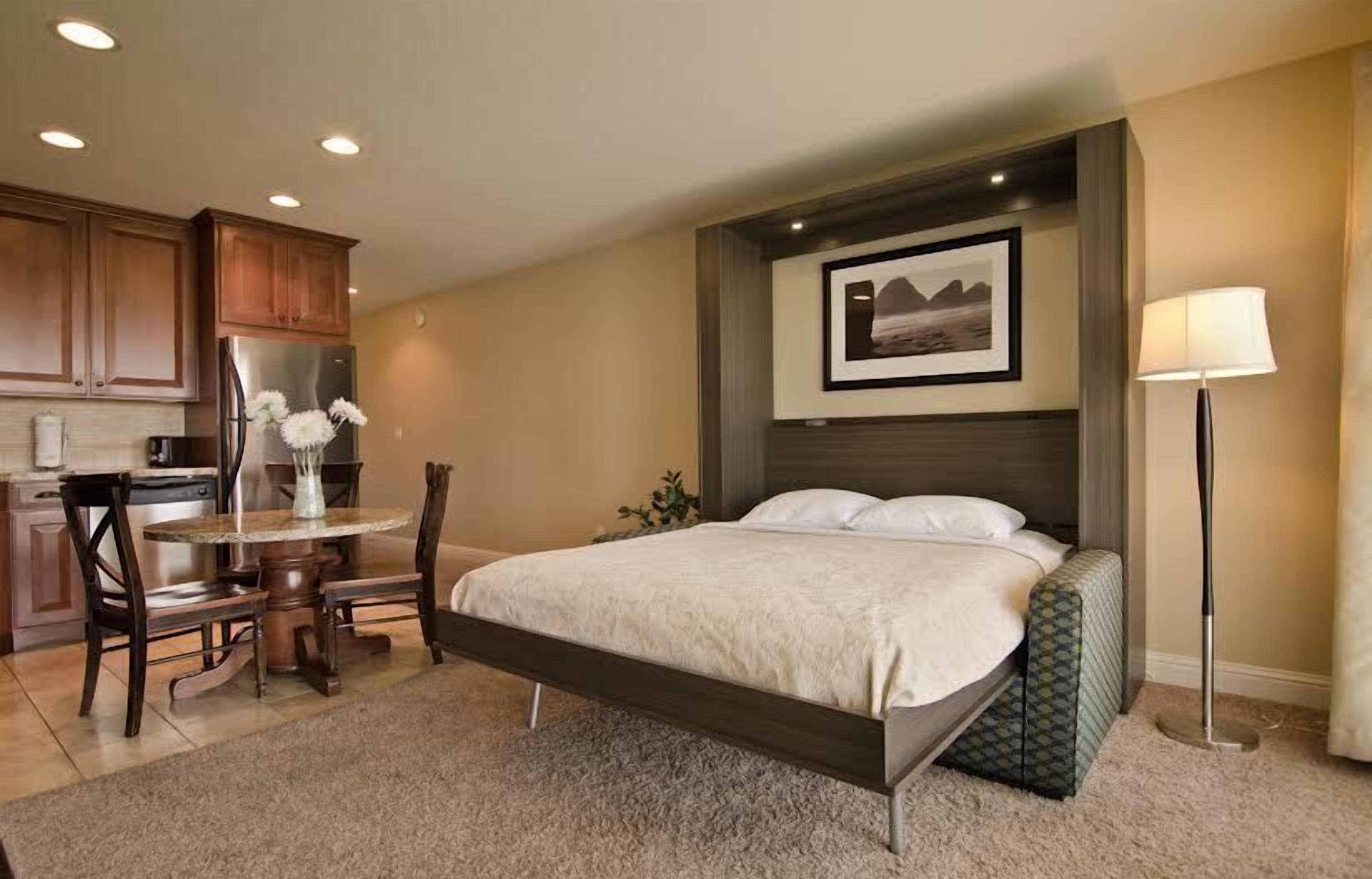 A hotel room with a bed, a desk, and a kitchenette.