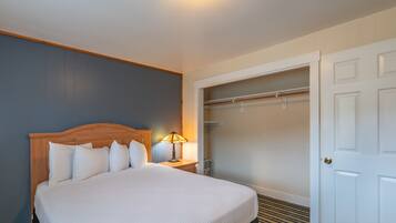 Quarto de hotel com cama grande, mesa de cabeceira com abajur, closet espaçoso e uma porta.