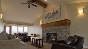 A spacious living room with a stone fireplace, leather sofas, and a ceiling fan. - Pacific Reef Hotel & Light Show (Gold Beach)