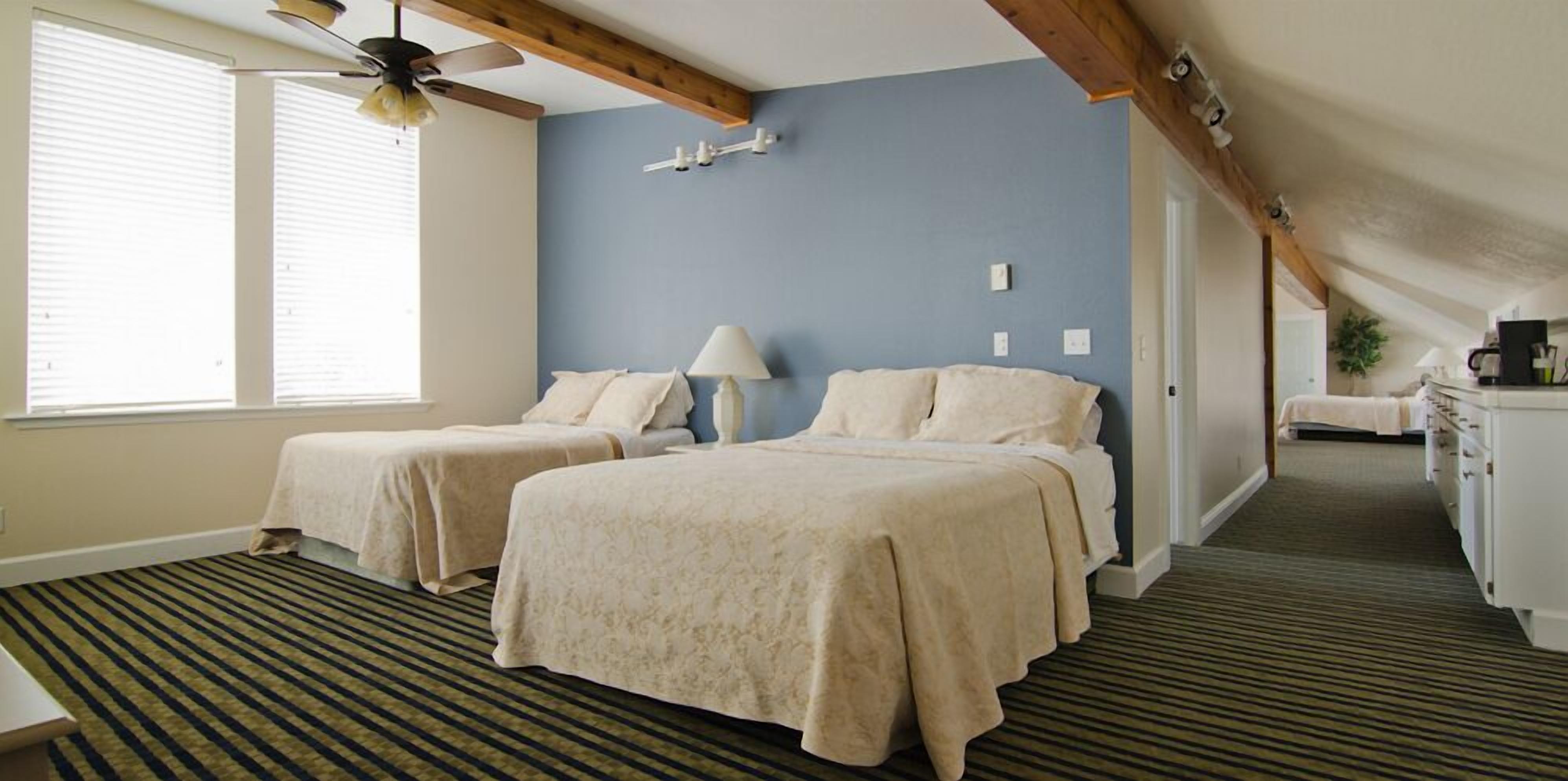 A hotel room with two beds, a ceiling fan, a lamp, and a view of the hallway.