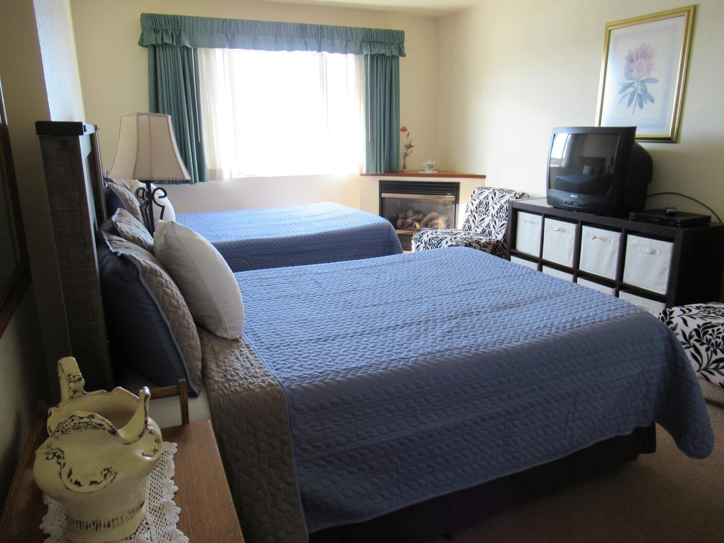 A hotel room with two beds, a television, a fireplace, and a framed picture on the wall.