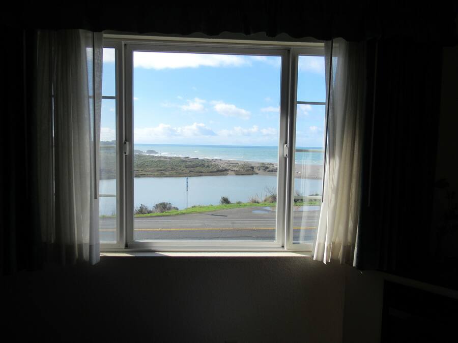 A room with a large window offering a view of a beach and ocean.