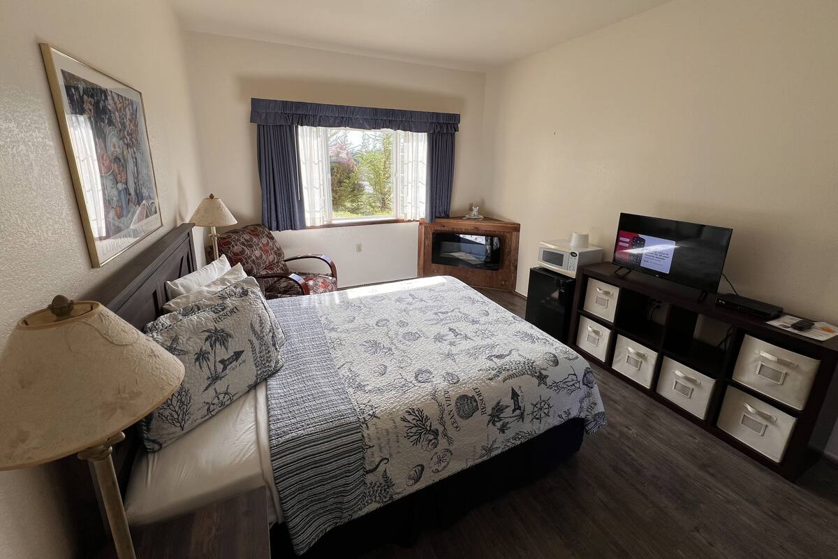 Ein Hotelzimmer mit einem Bett, einem Schreibtisch mit Computer, einem Fernseher und einem Fenster mit Vorhängen.