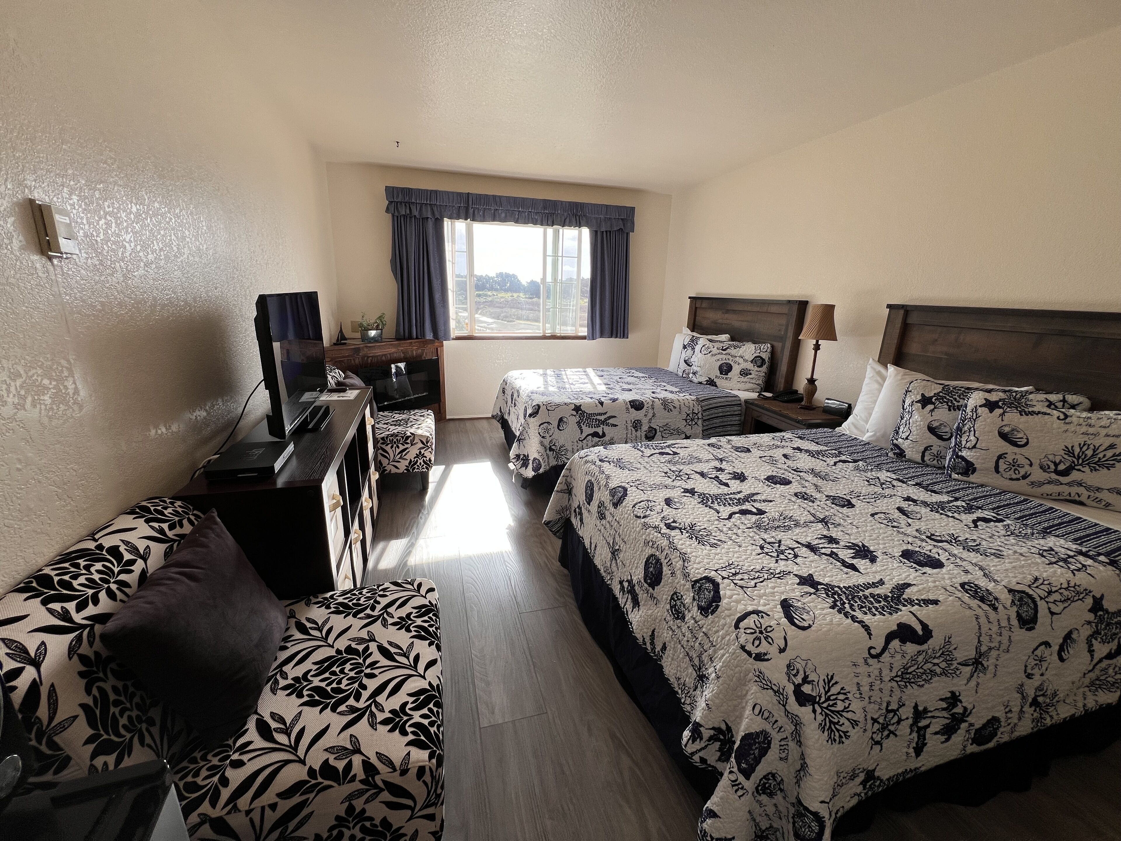 A hotel room with two beds, a desk with a TV, a chair, and a window with curtains.