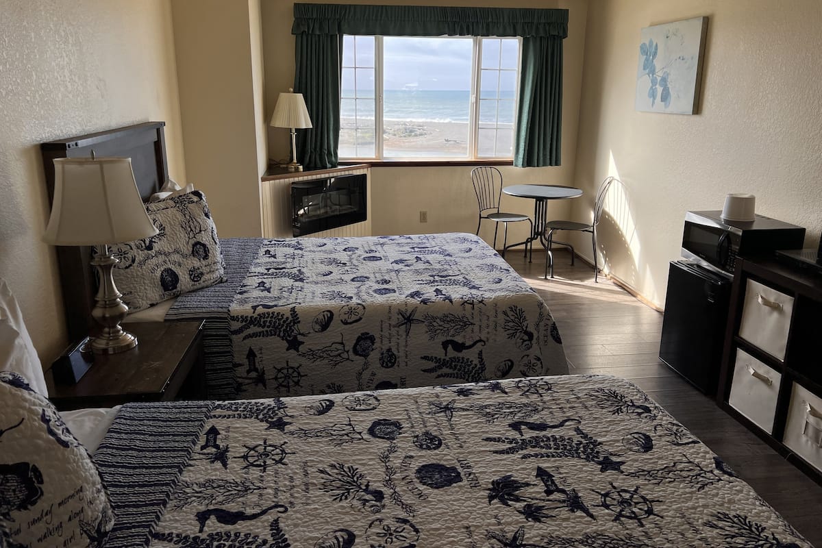 Ein Hotelzimmer mit zwei Betten, einem Schreibtisch, einem Sessel und Meerblick.