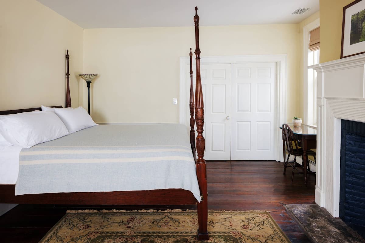 A four-poster bed with a wooden headboard, a white door, a small table with chairs, and a fireplace.