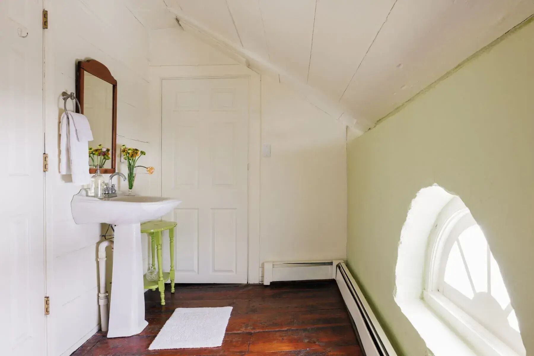 A bathroom with a white sink, a mirror, a green stool, and a white door.