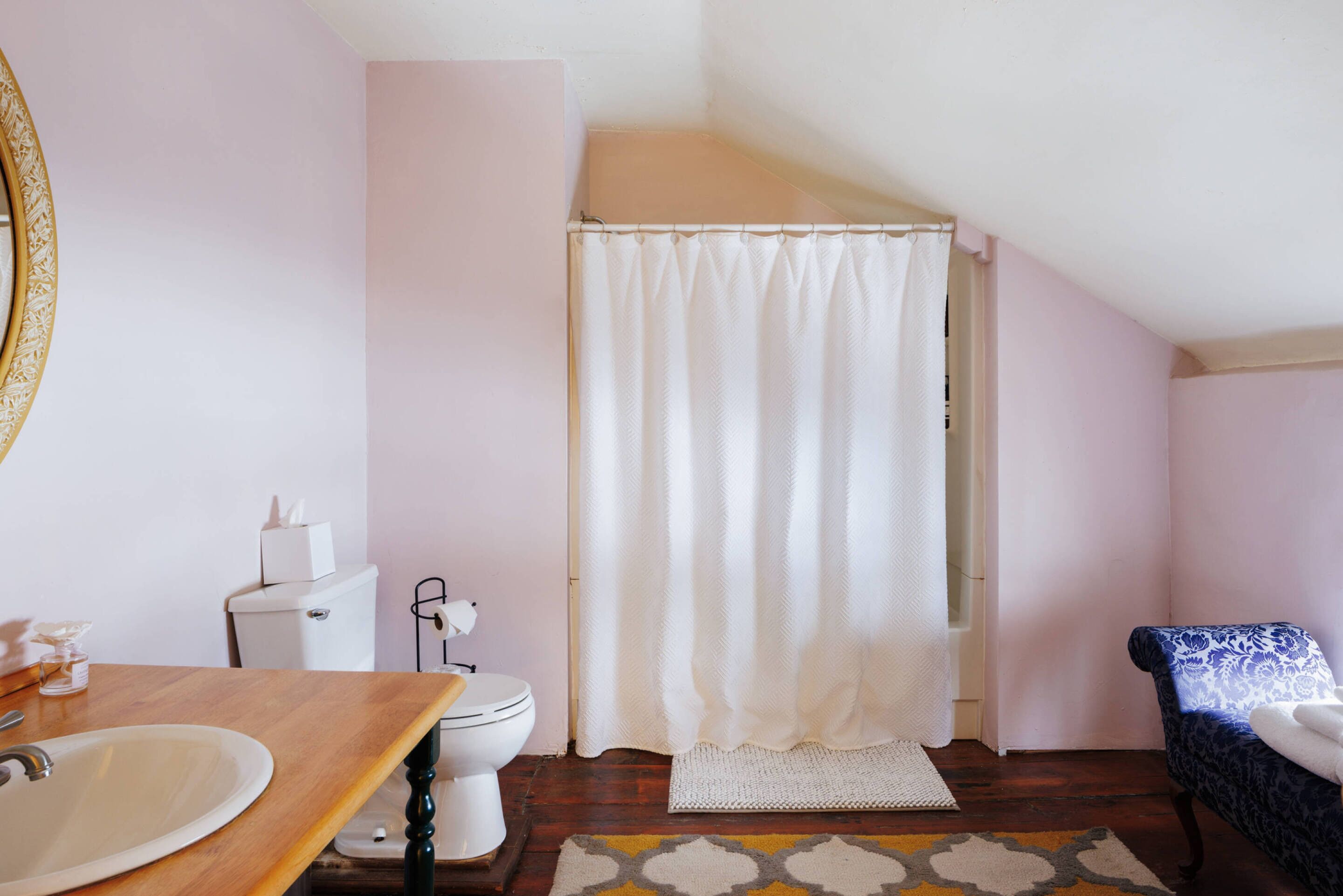 Un baño con tocador de madera, inodoro blanco, cortina de ducha y alfombra estampada.